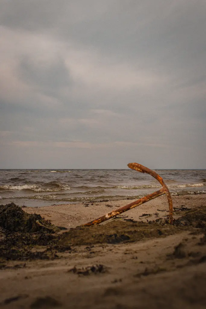 Rusty anchor lying on sandy beach by the sea. Image depicting anchor.
