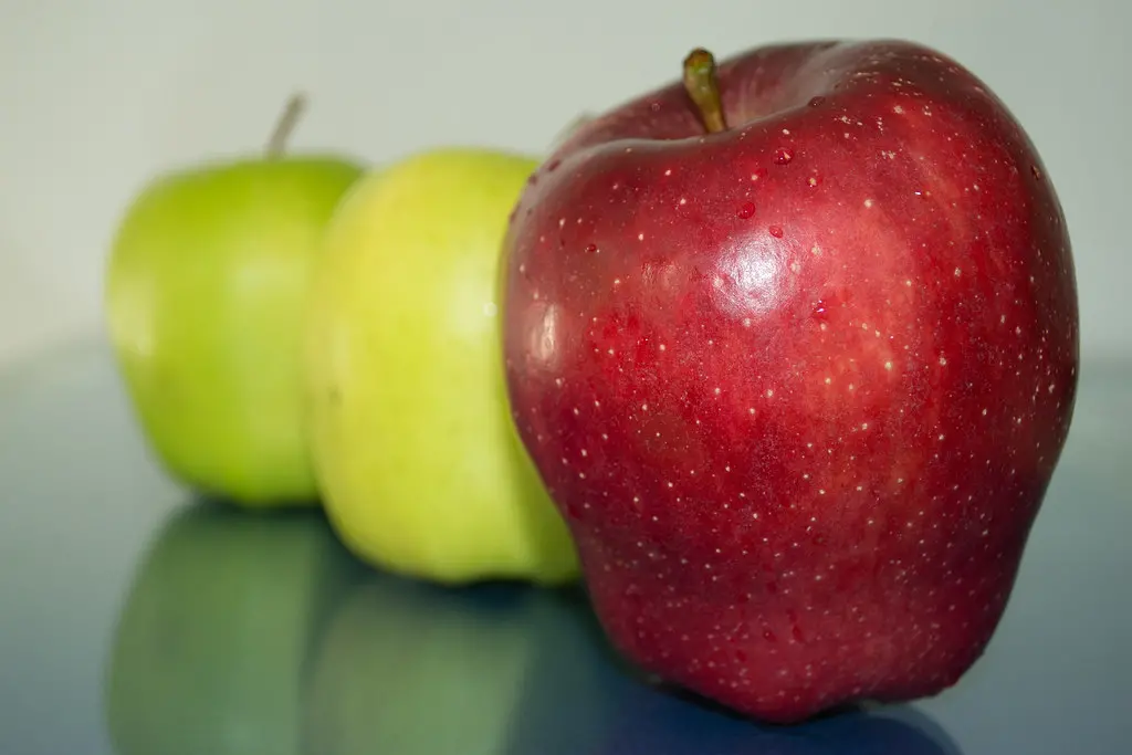 Three apples, two green and one red, on a table. Picture showing apple.