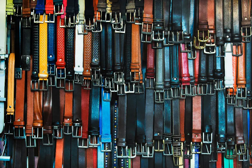 Colorful belts with shiny buckles hanging in a row. Image depicting buckle.