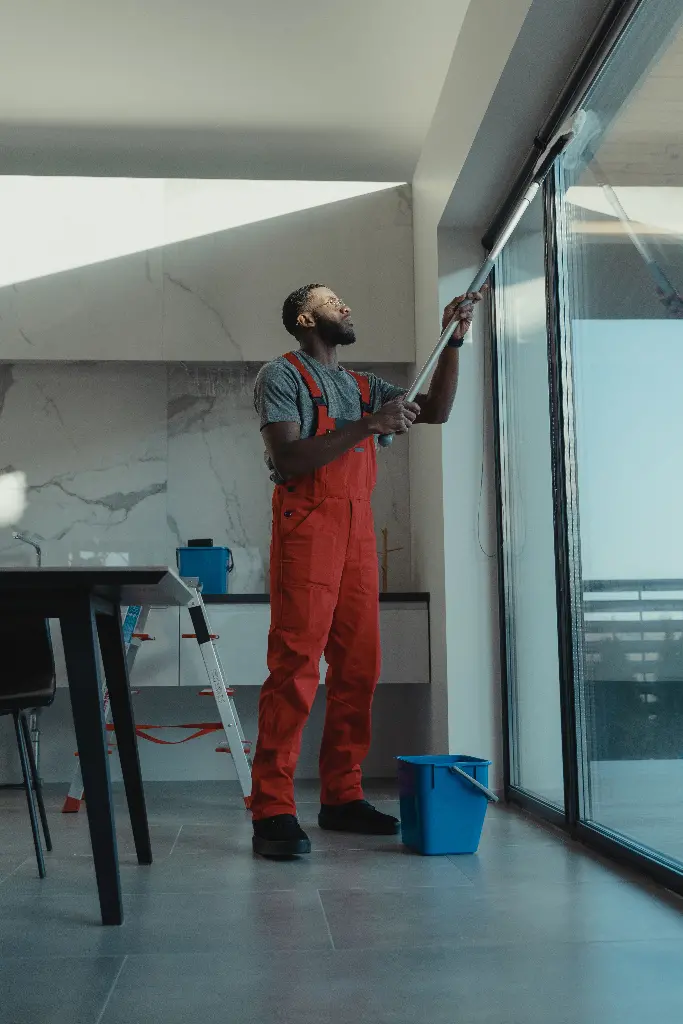 Person in red overalls cleaning large window with squeegee. Image depicting cleaning.