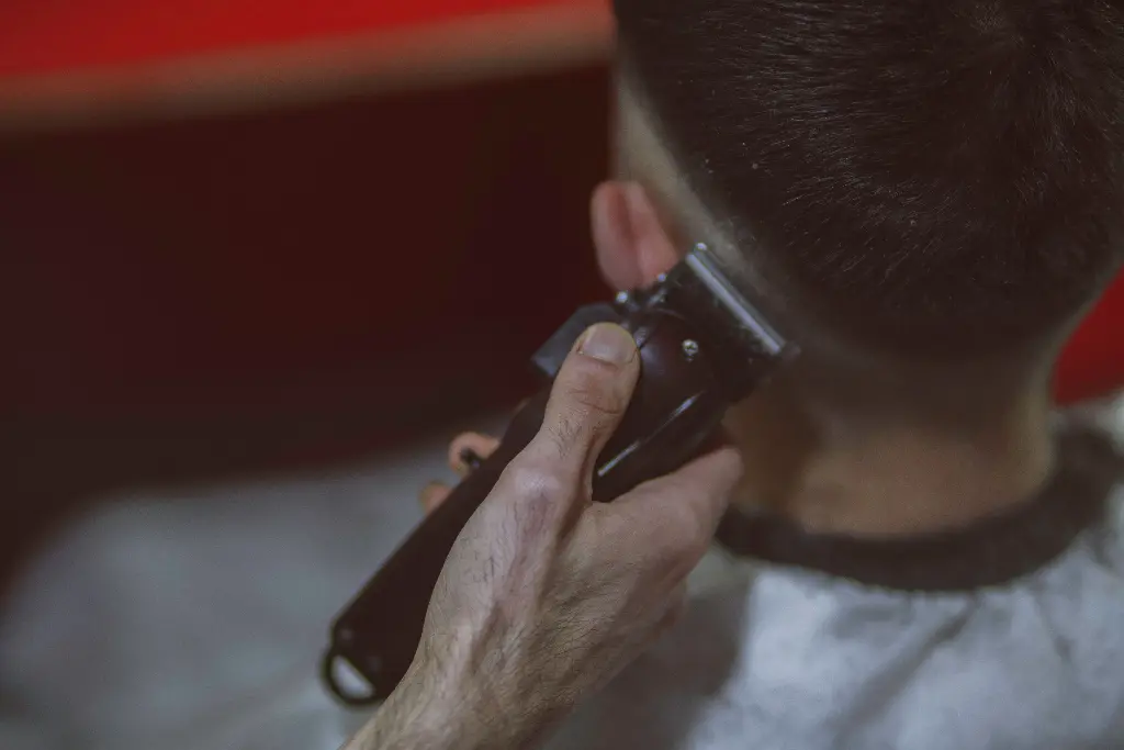Person using clippers to trim hair at a barbershop. Image depicting clippers.