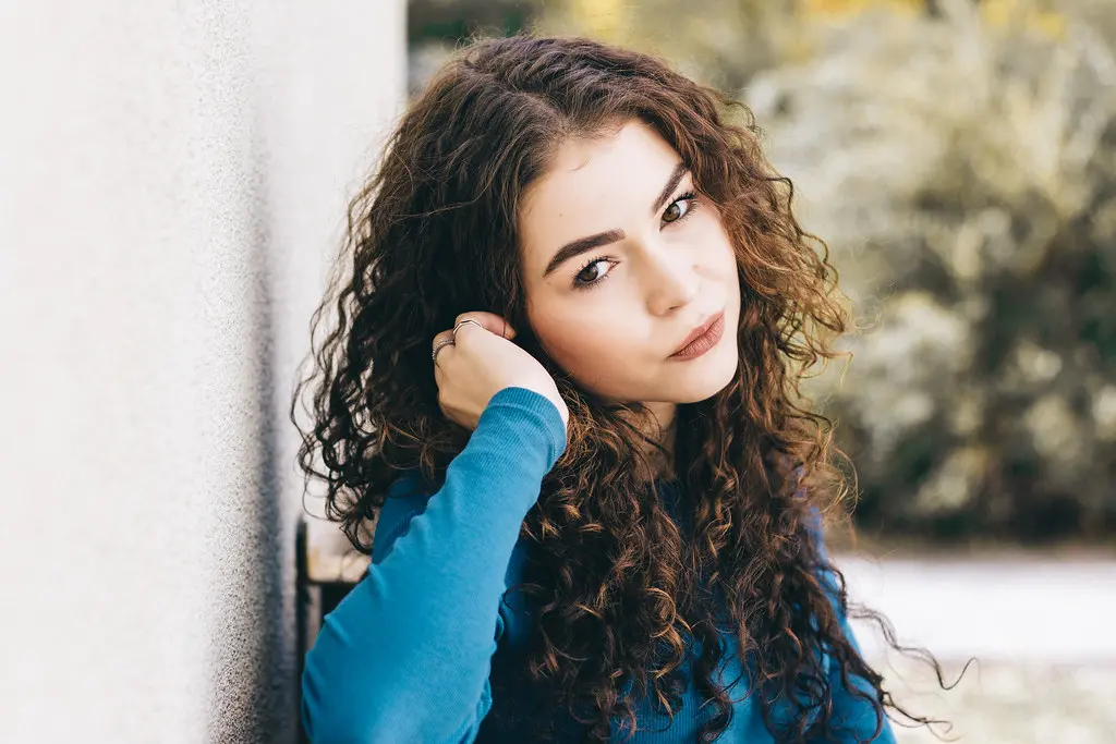 Girl with curly hair wearing blue sweater outdoors Image depicting curly.