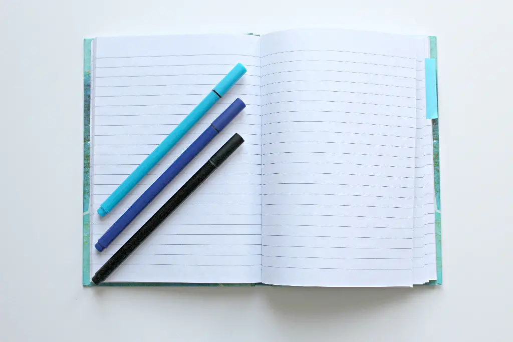 Open diary with lined pages and colorful pens on top. Image depicting diary.
