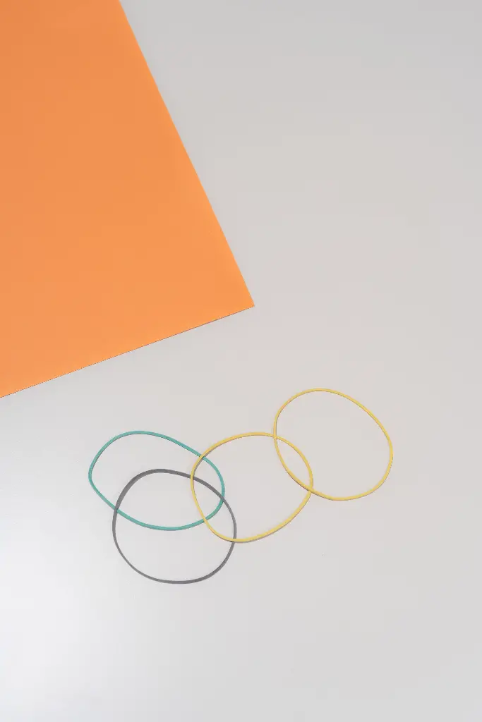 Colorful elastic bands next to orange paper on table. Image depicting elastic.
