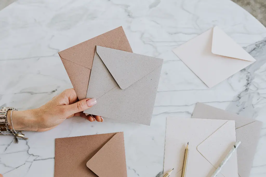 Person holding brown and gray envelopes on table. Image depicting envelope.