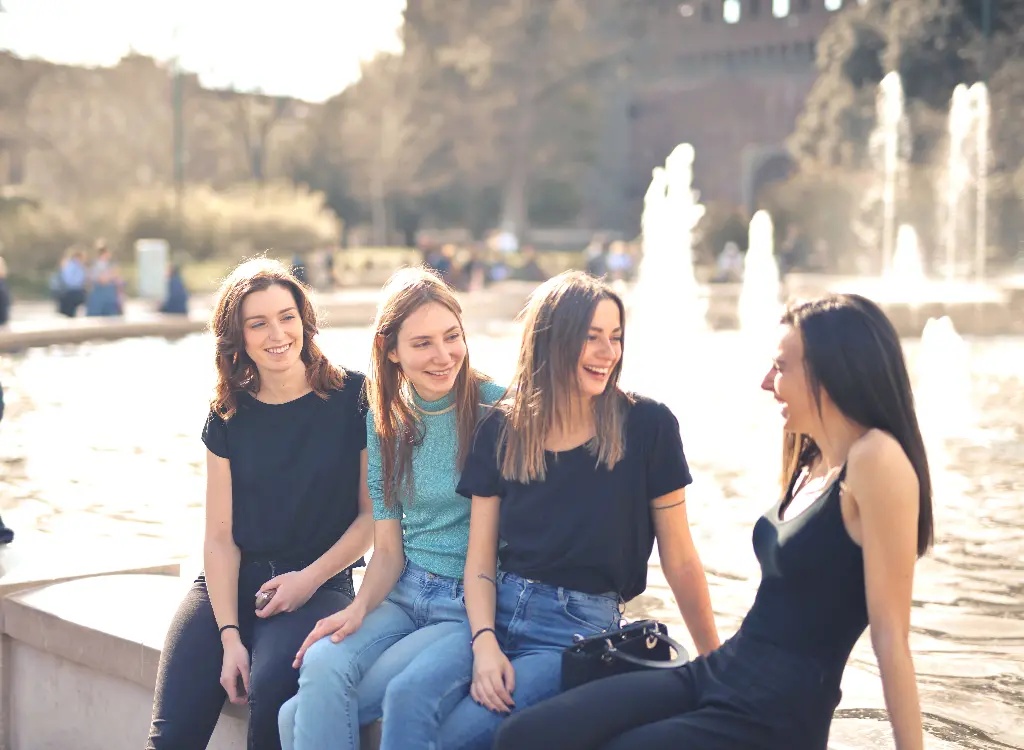 Four friends laughing together by a fountain. Image depicting friend.
