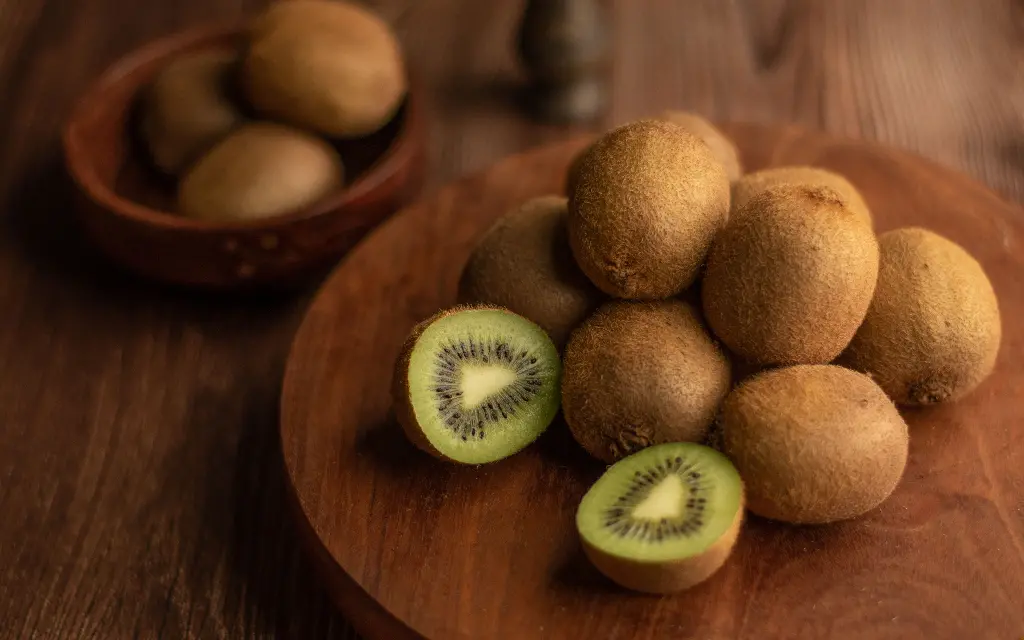 Pile of whole and sliced kiwis on wooden board. Image depicting kiwi.