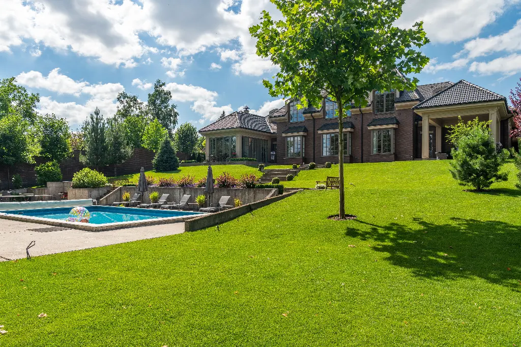 Large green lawn with a pool and house in the background. Image depicting lawn.