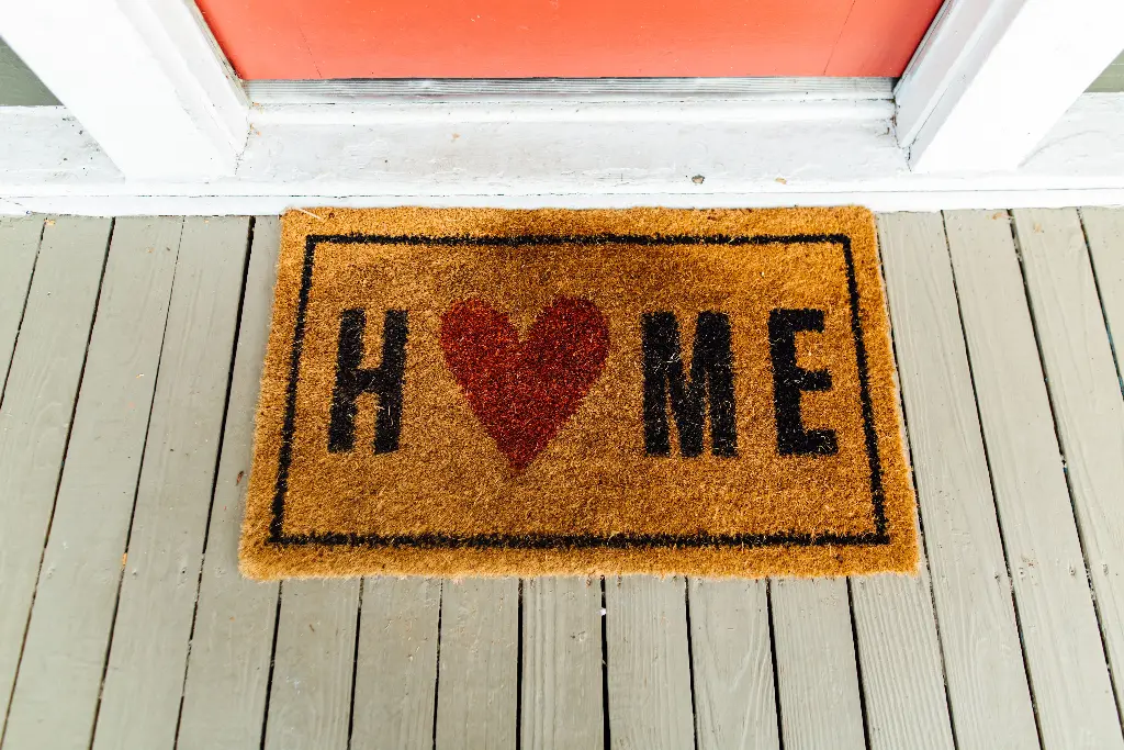 Welcome mat with heart symbol spelling home on porch Image depicting mat.