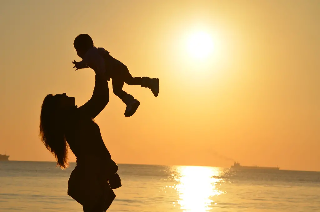Mother lifting child at sunset by the sea. Image depicting mum.