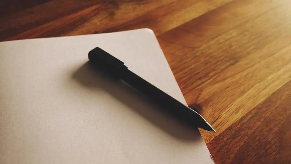 Black pen on blank notepad on wooden table Image depicting pad.