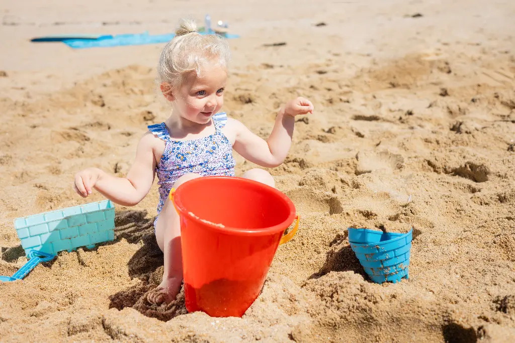 Child playing with red pail on sandy beach. Image depicting pail.