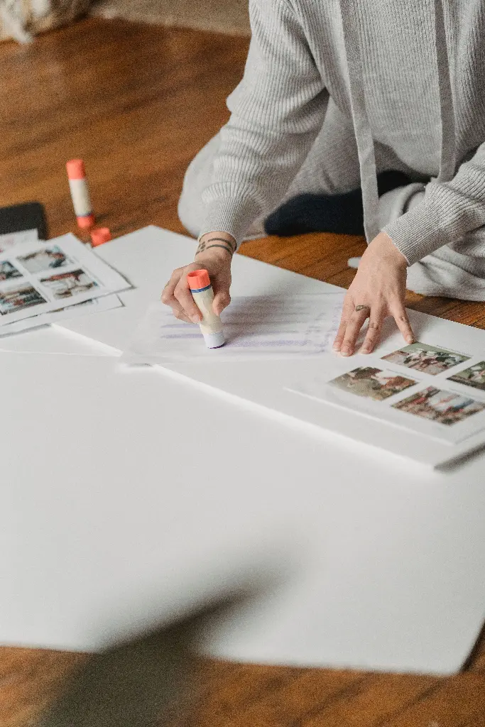Person using glue stick to paste photos on paper Image depicting paste.