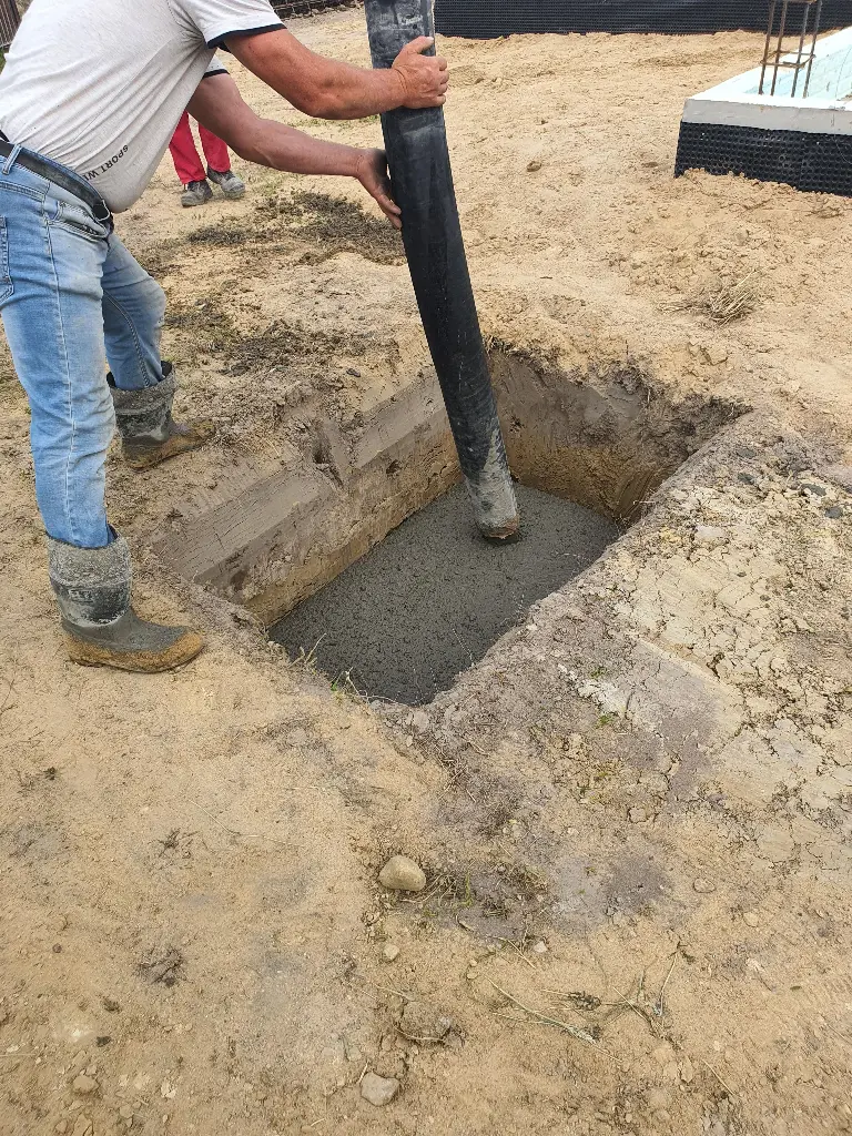 Worker pouring concrete into a pit on construction site. Image depicting pit.