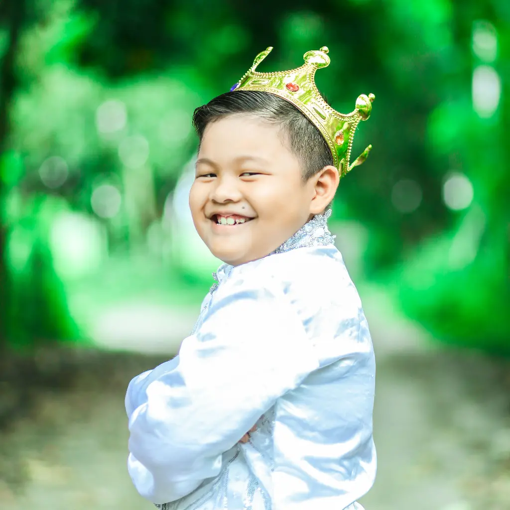 Smiling boy wearing a crown, dressed as a prince. Image depicting prince.