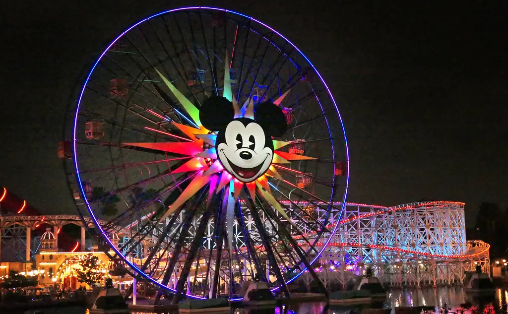 Colorful Ferris wheel with cartoon face at night amusement park. Image depicting queue.