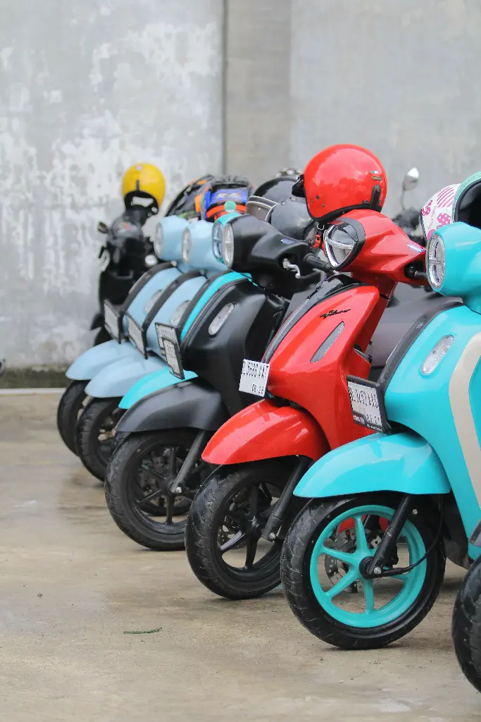 Colorful scooters parked in a row outside. Image depicting scooter.