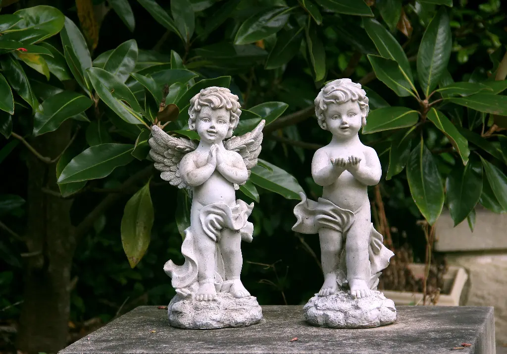 Two angel statues in a garden setting. Image depicting statues.