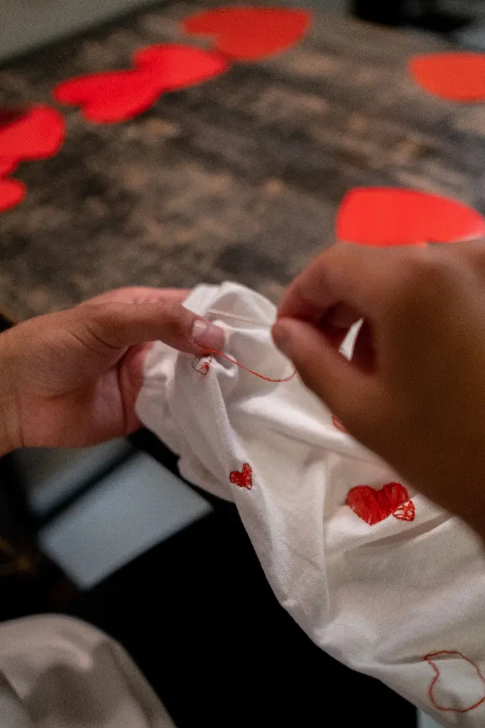 Hands stitching red hearts on white fabric. Image depicting stitch.