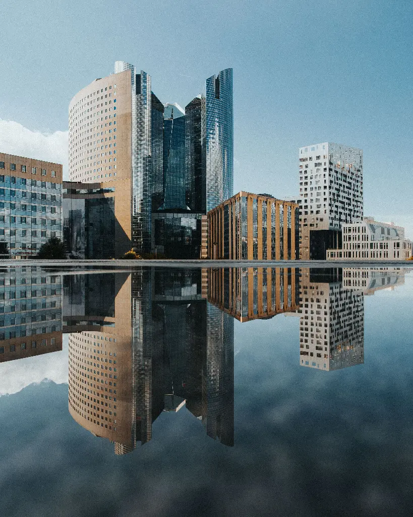 Modern skyscrapers reflecting in calm water, showcasing urban structures. Image depicting structures.
