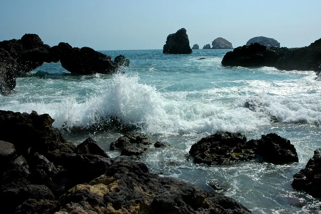Ocean waves crashing on rocky shore, creating surf. Image depicting surf.