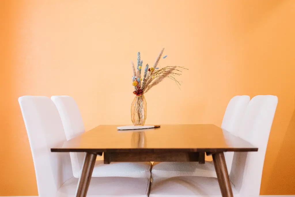 Wooden table with white chairs and vase on top Image depicting tables.