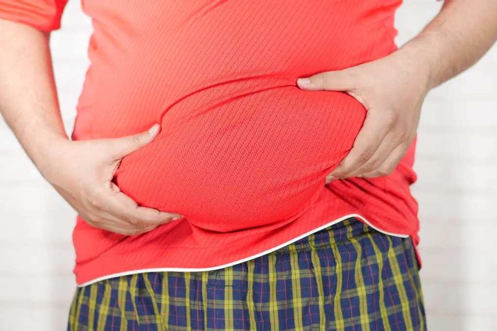 Person holding their round tummy in red shirt. Image depicting tummy.