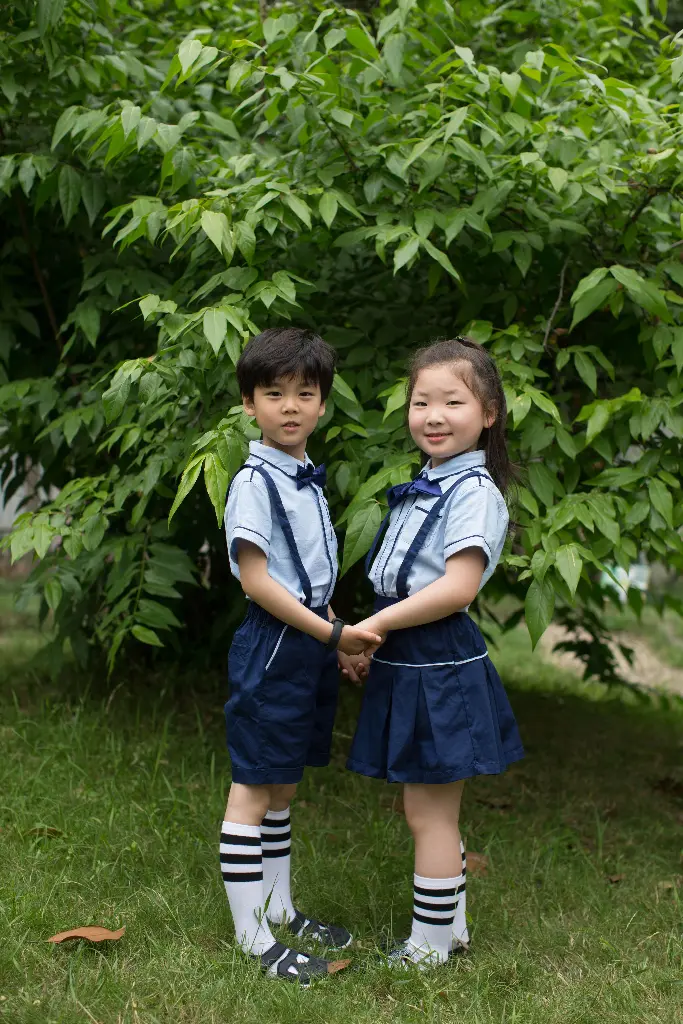 Two children in school uniforms standing together outdoors. Image depicting uniform.