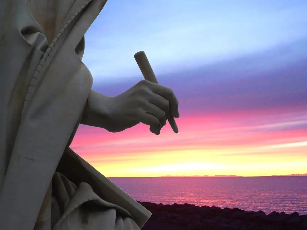 Statue hand holding pen against colorful sunset wallpaper. Image depicting wallpaper.